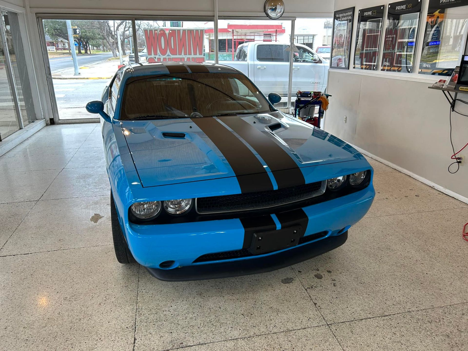 Blue Dodge Challenger with black racing stripes inside a shop, facing the camera.