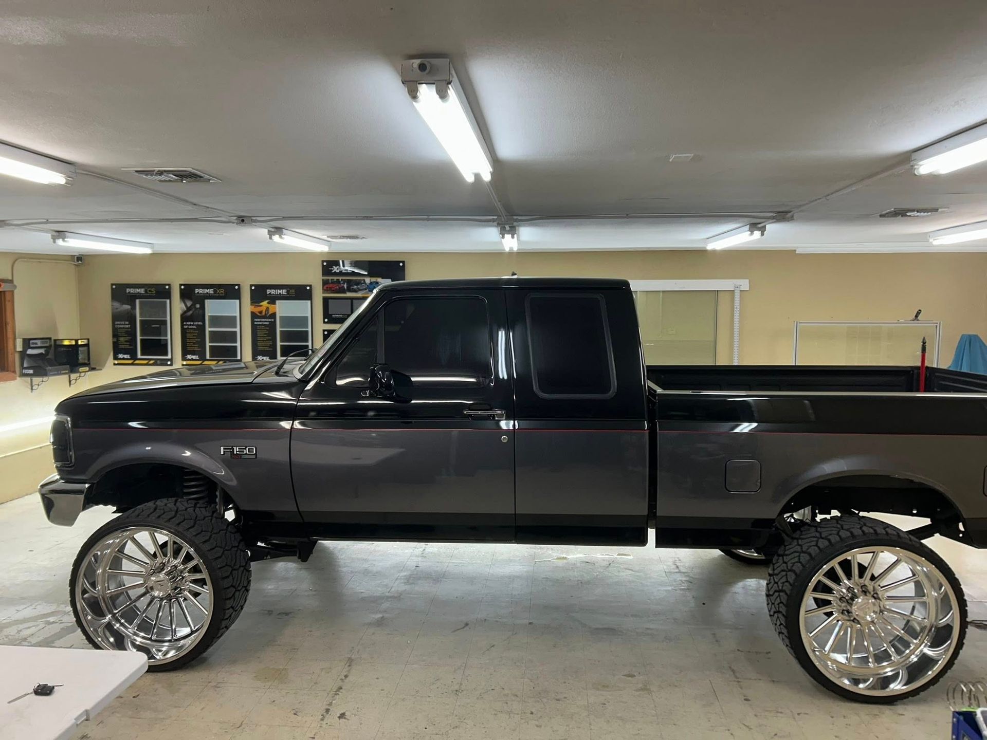 Gray and black lifted Ford pickup truck with chrome wheels inside a garage.