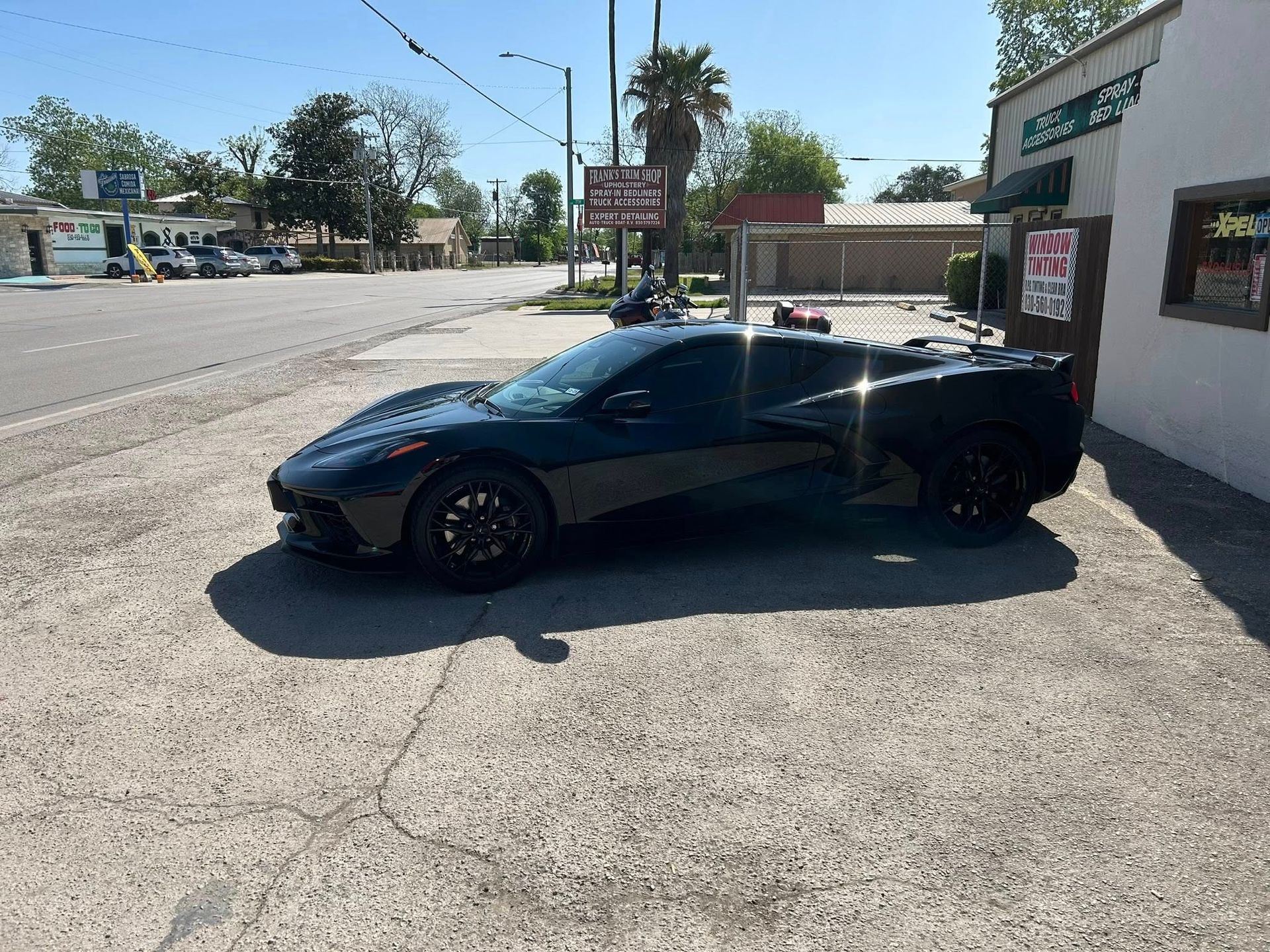 Black sports car parked next to a building on a sunny street.