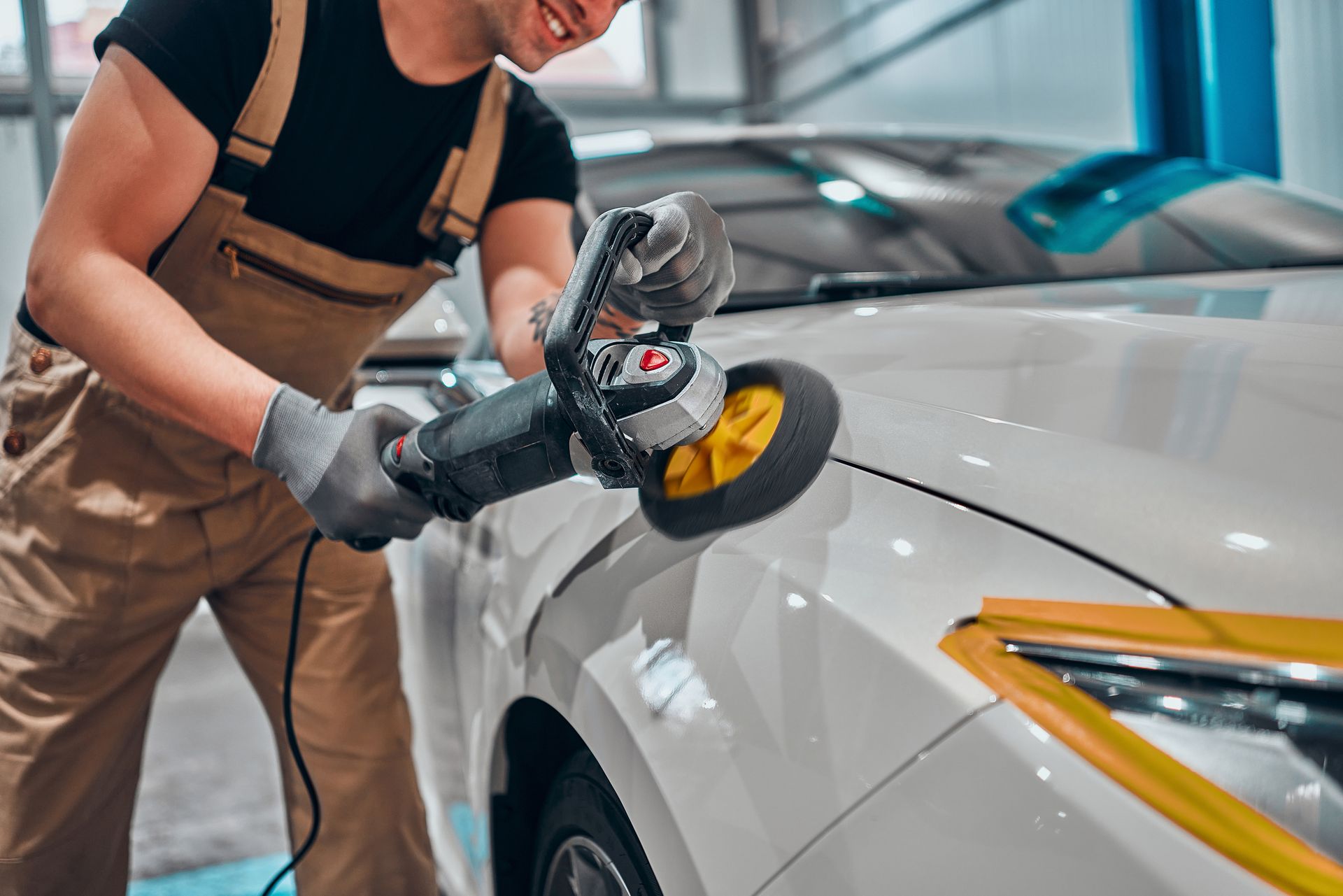 Mechanic using a polisher on a white car in a garage.