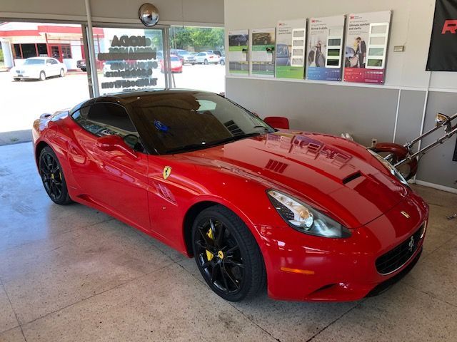 Red Ferrari sports car with black roof, wheels, and yellow brake calipers, in a garage.