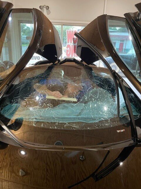 A person in a wooden hot tub, with glass and wood surrounding the tub, outdoors.