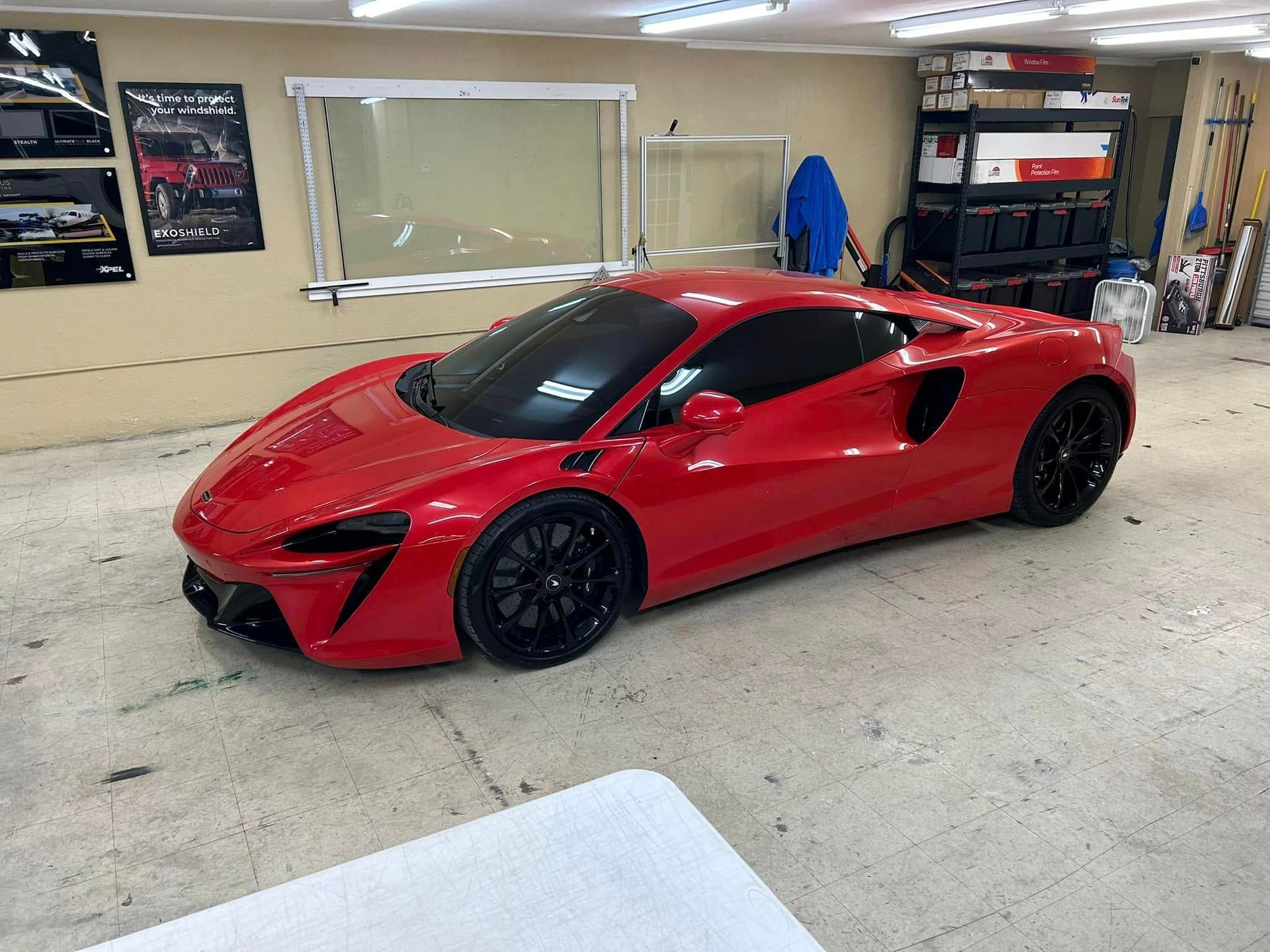 Red McLaren sports car in a garage, black wheels, tinted windows.