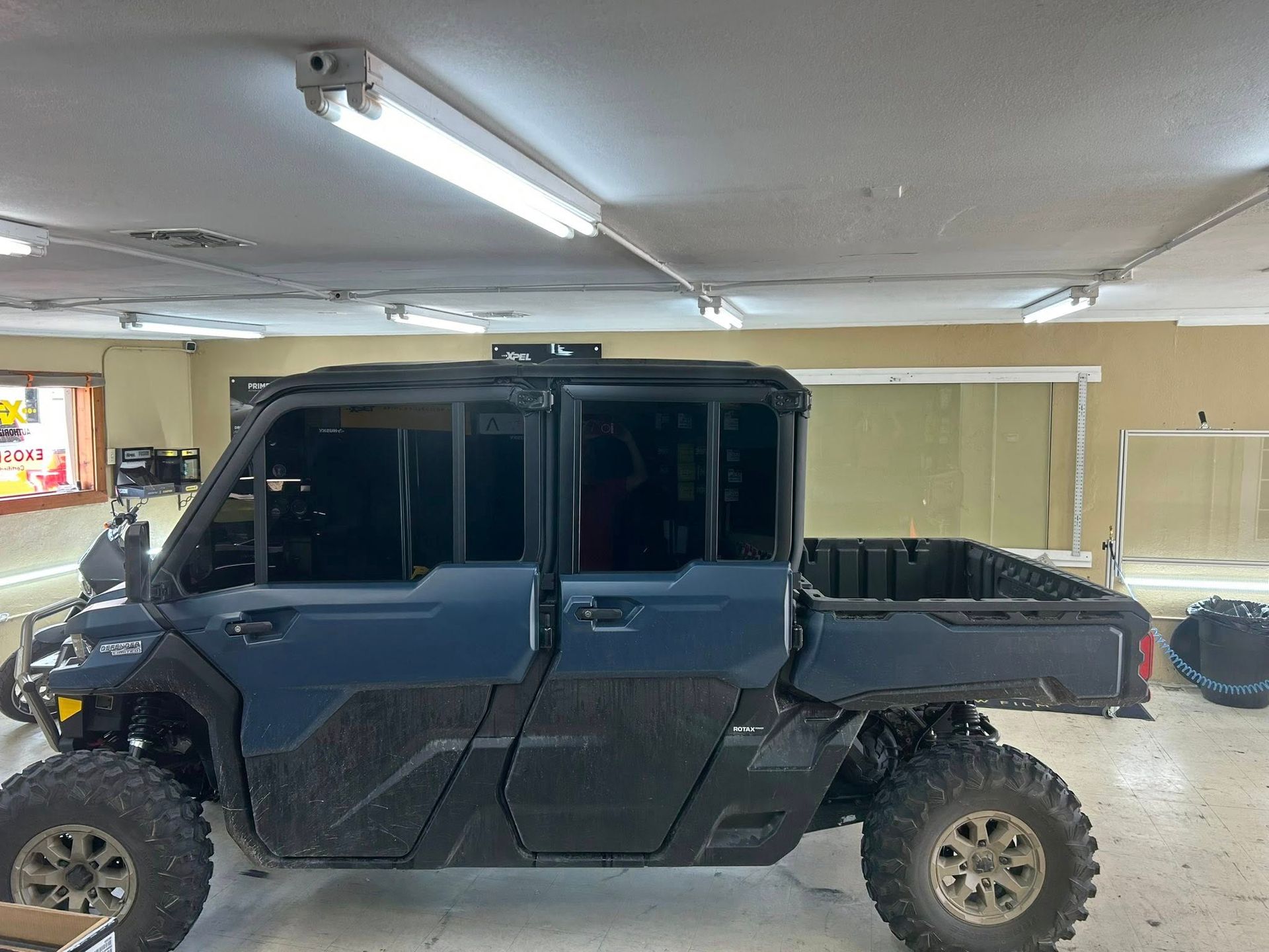 Blue utility terrain vehicle parked inside a garage with tinted windows, and a cargo bed.