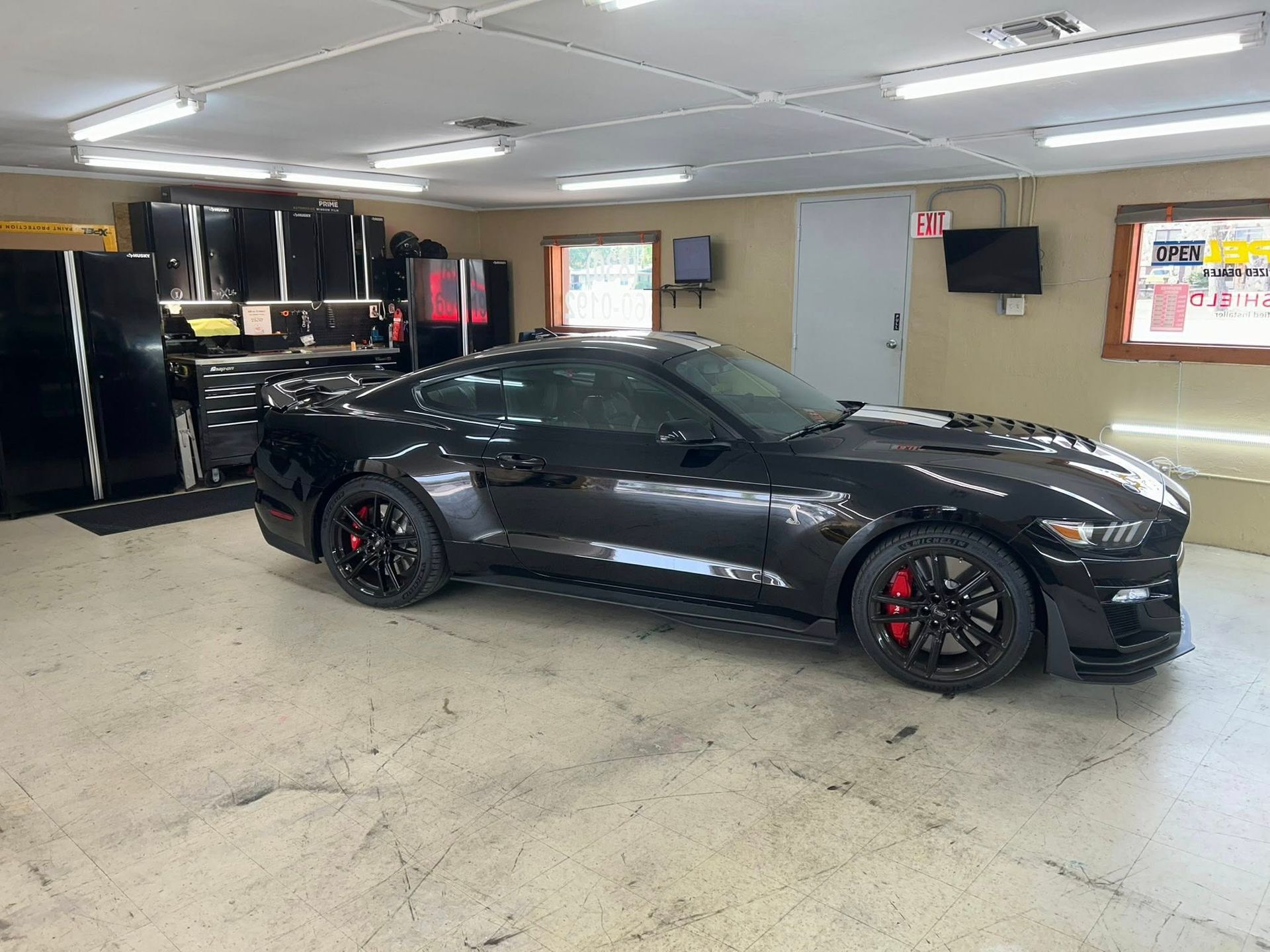 Black sports car in garage with black cabinets and red brake calipers.