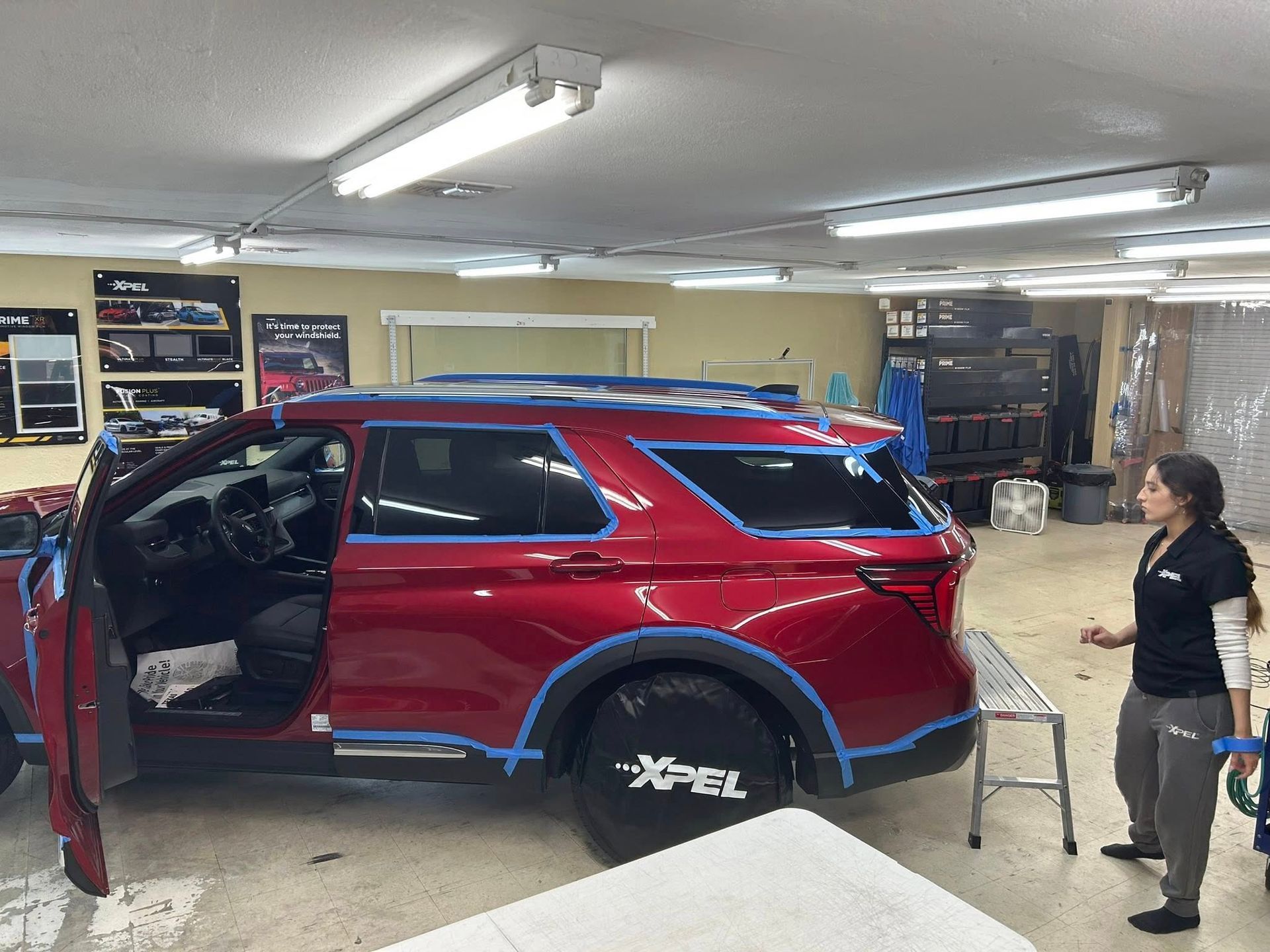 Red SUV in a shop being worked on by a person. Blue tape outlines panels.