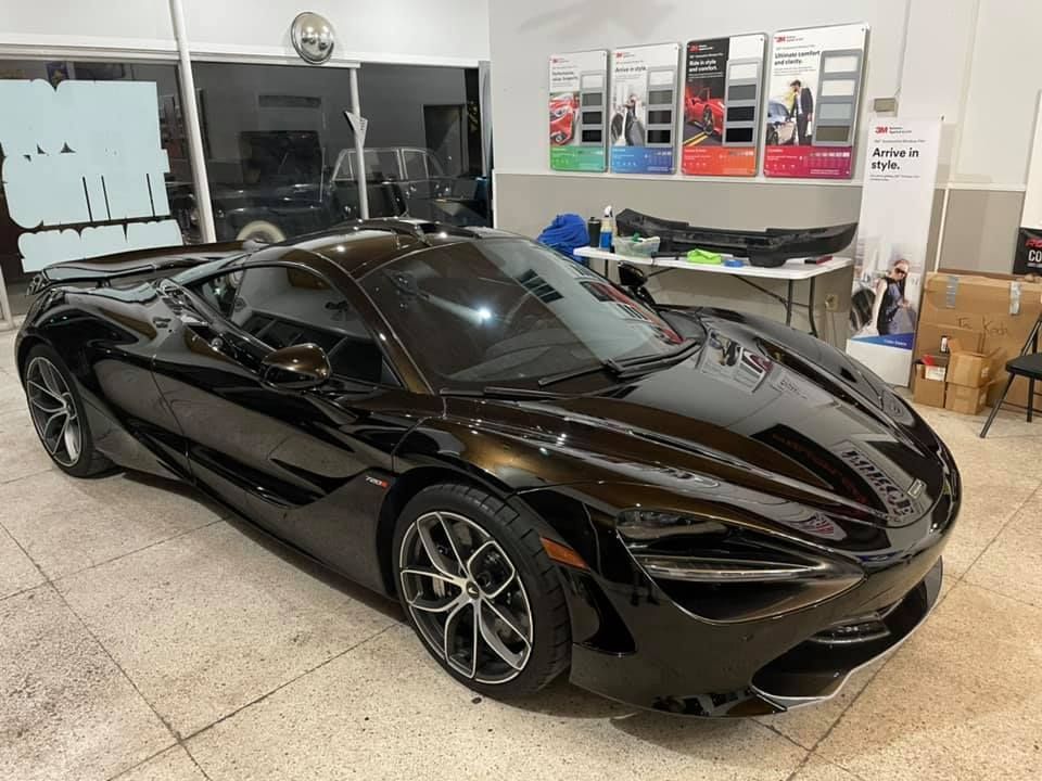 Black McLaren sports car parked inside a shop, with tinting samples and tools in the background.