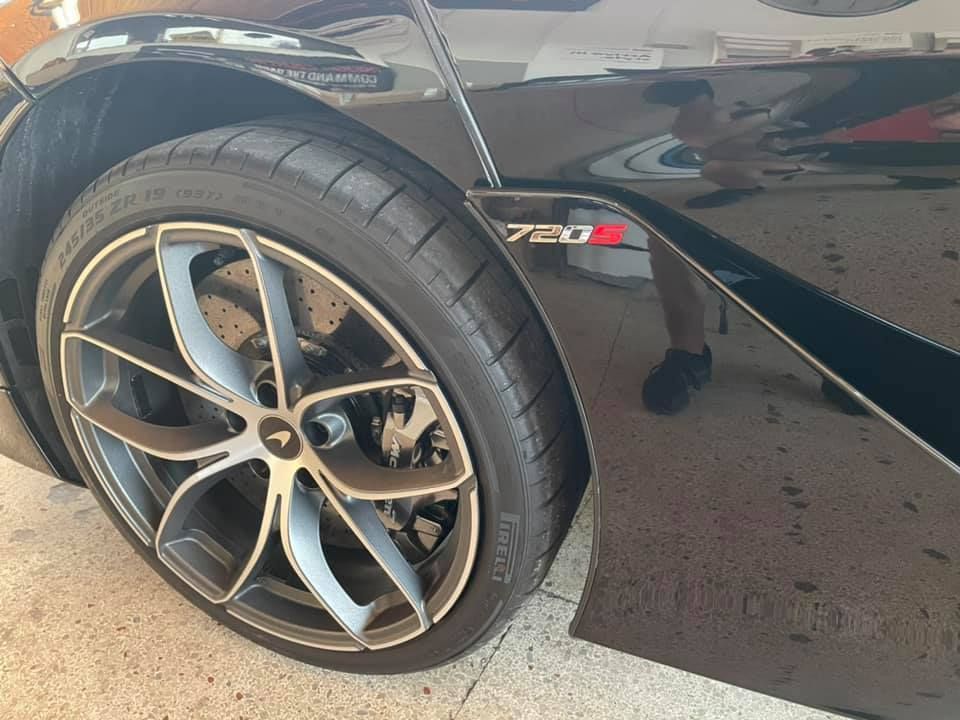 Black McLaren 720S sports car; front wheel and body detail. Silver and black rim, tire, and 