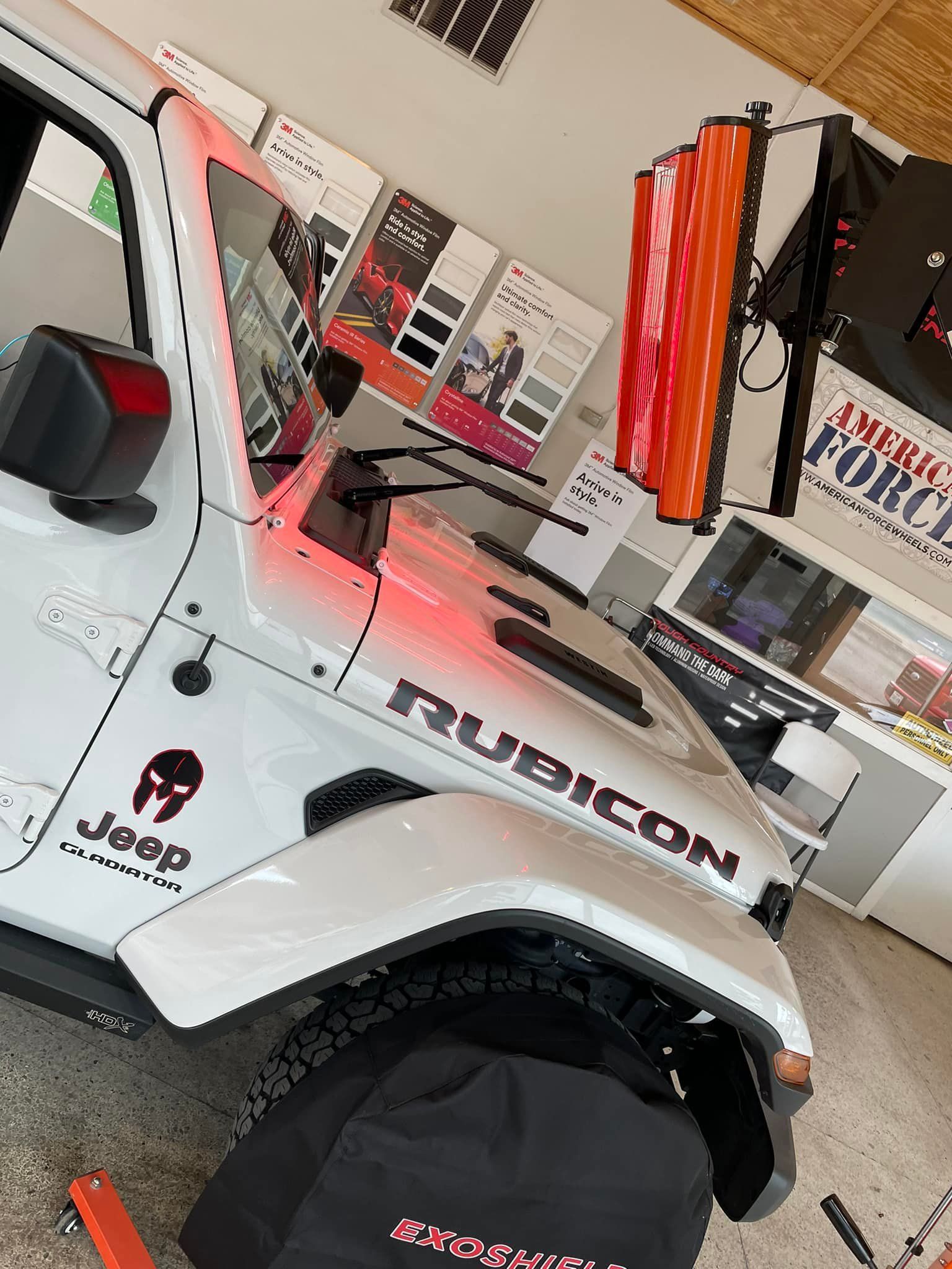 White Jeep Wrangler Rubicon with custom hood wrap. Displays, brochures, and wraps in a shop.