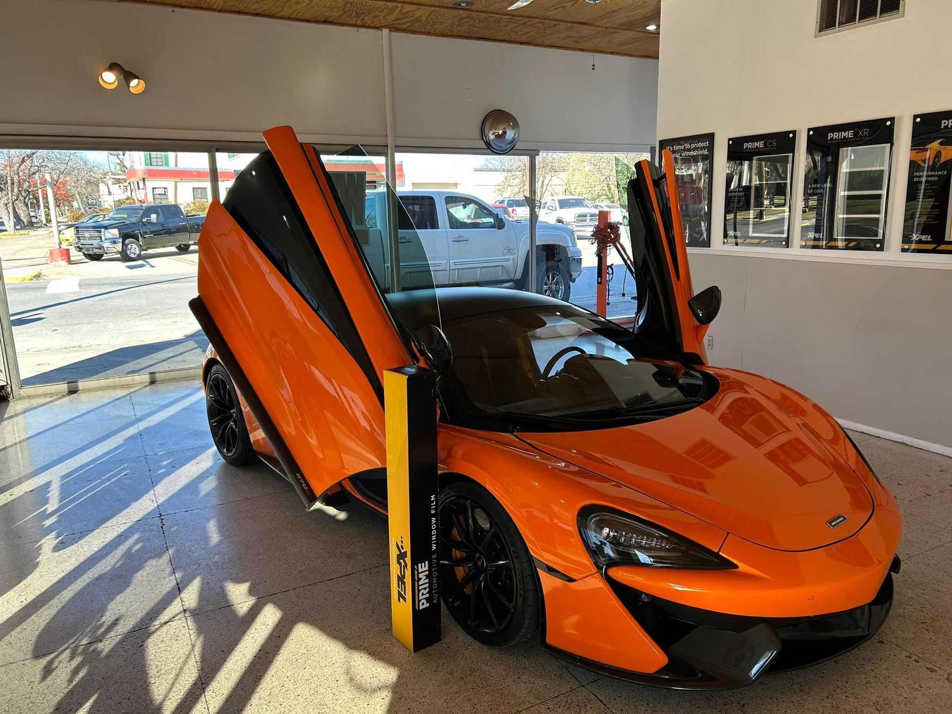 Bright orange McLaren sports car with doors open in a showroom.