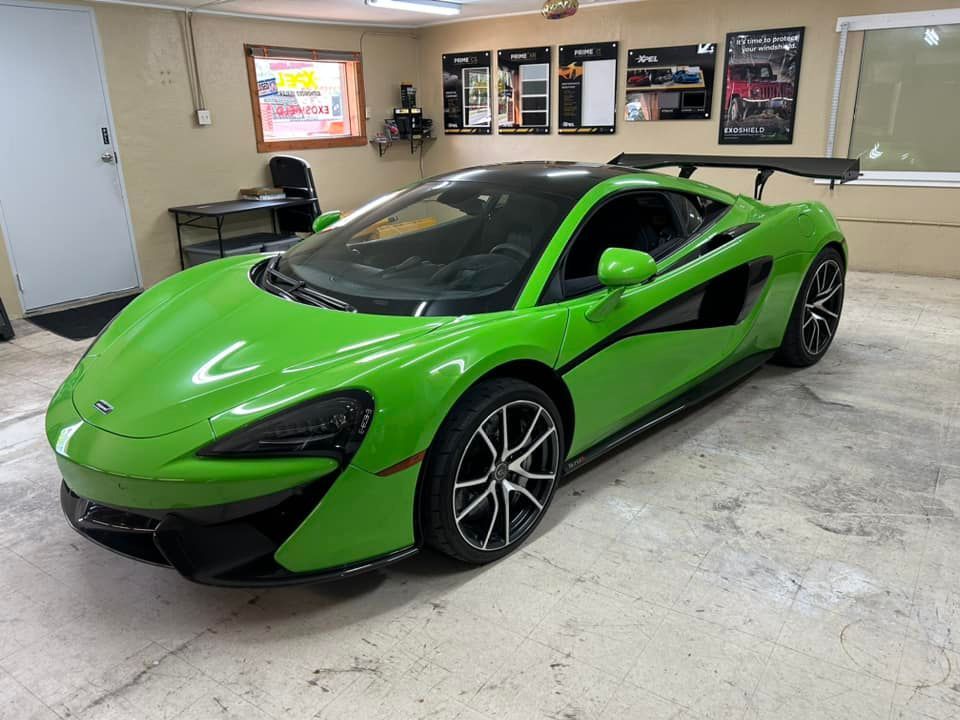 Bright green McLaren sports car in a garage setting, black accents, black wing, shiny.