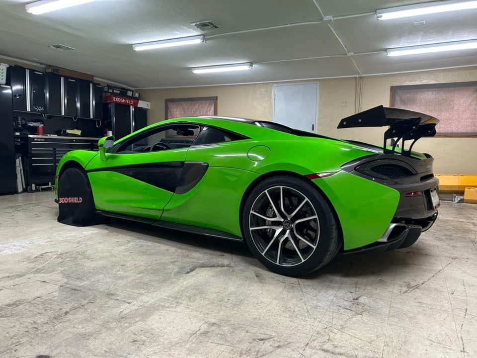 Green McLaren sports car in a garage, with black spoiler and black wheels.