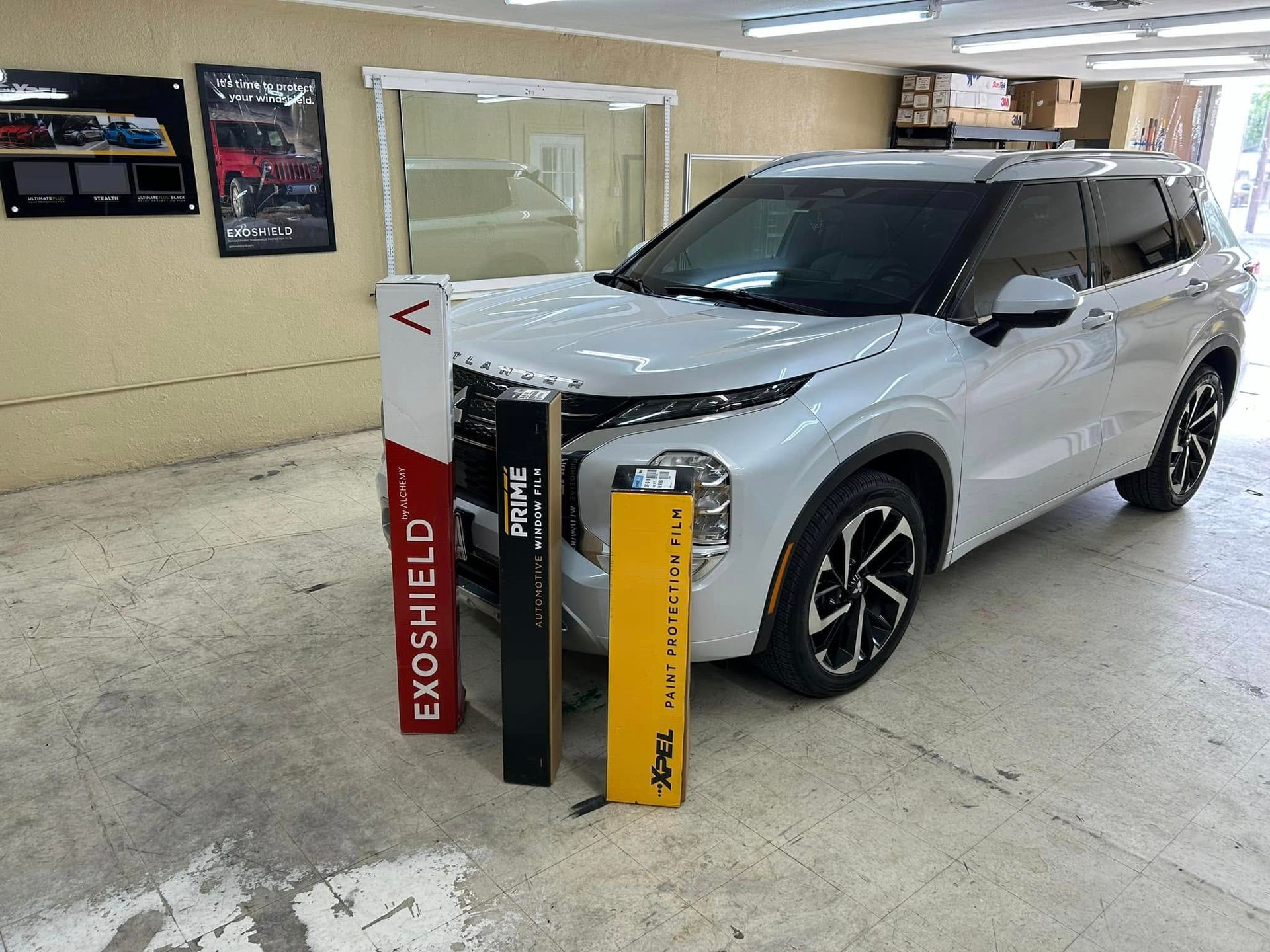 White SUV with protective film products displayed next to it inside a shop.