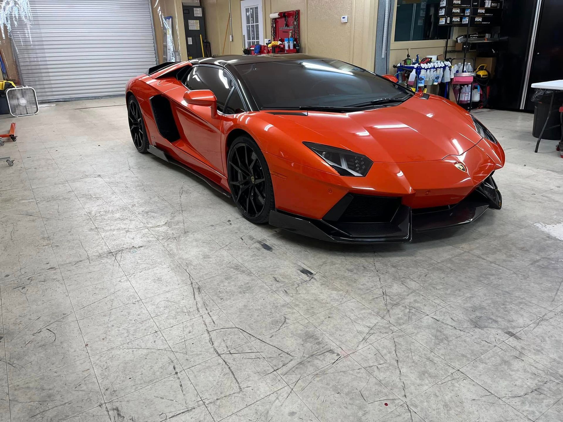 Orange Lamborghini Aventador in a garage, black accents, front view.