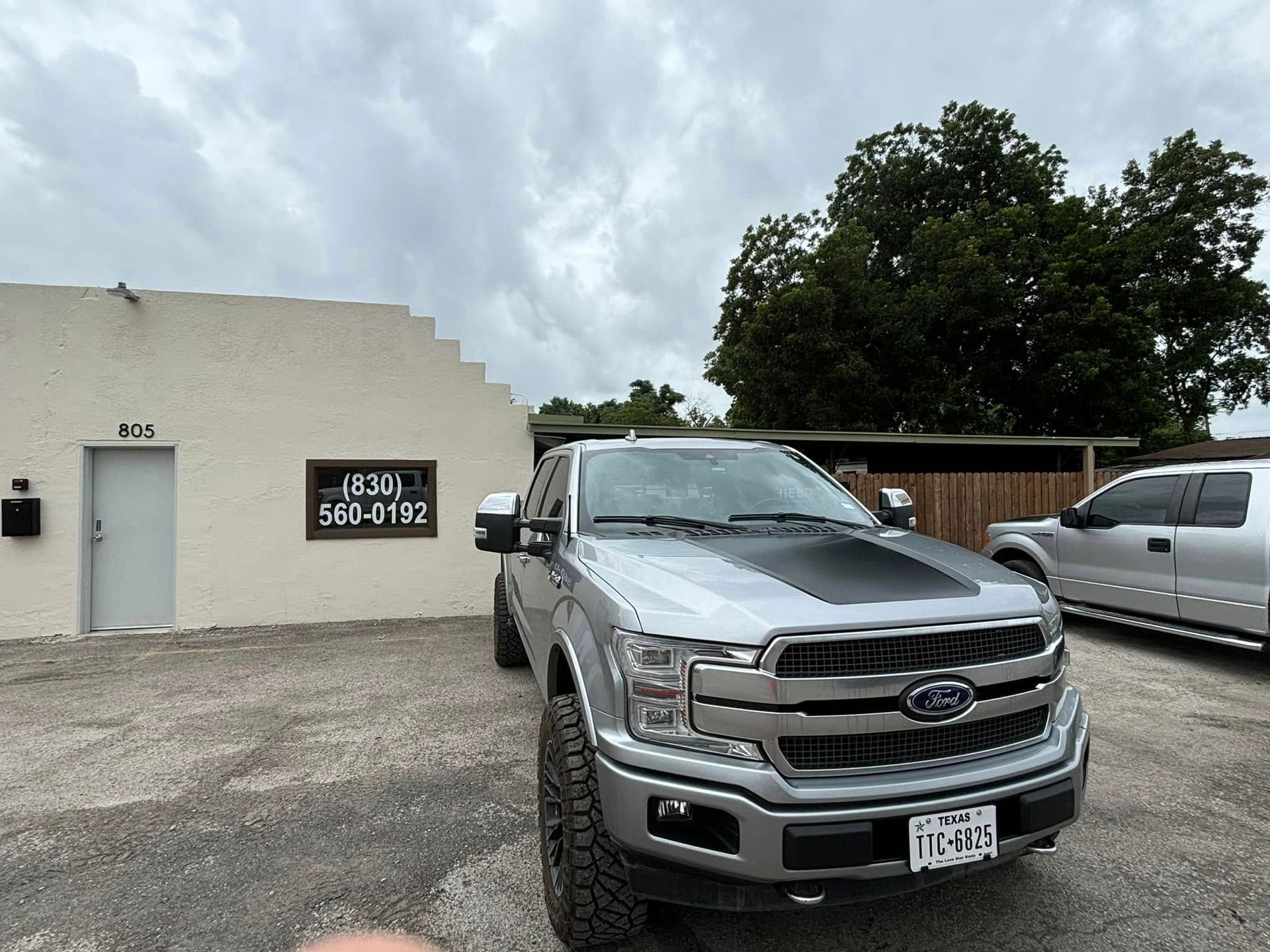 Silver Ford truck parked in front of a building with a sign and a gray sky.