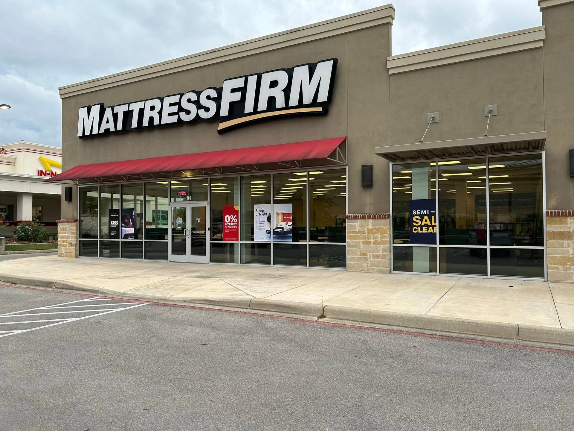 Mattress Firm store exterior with large sign, red awning, and glass windows in a shopping center.