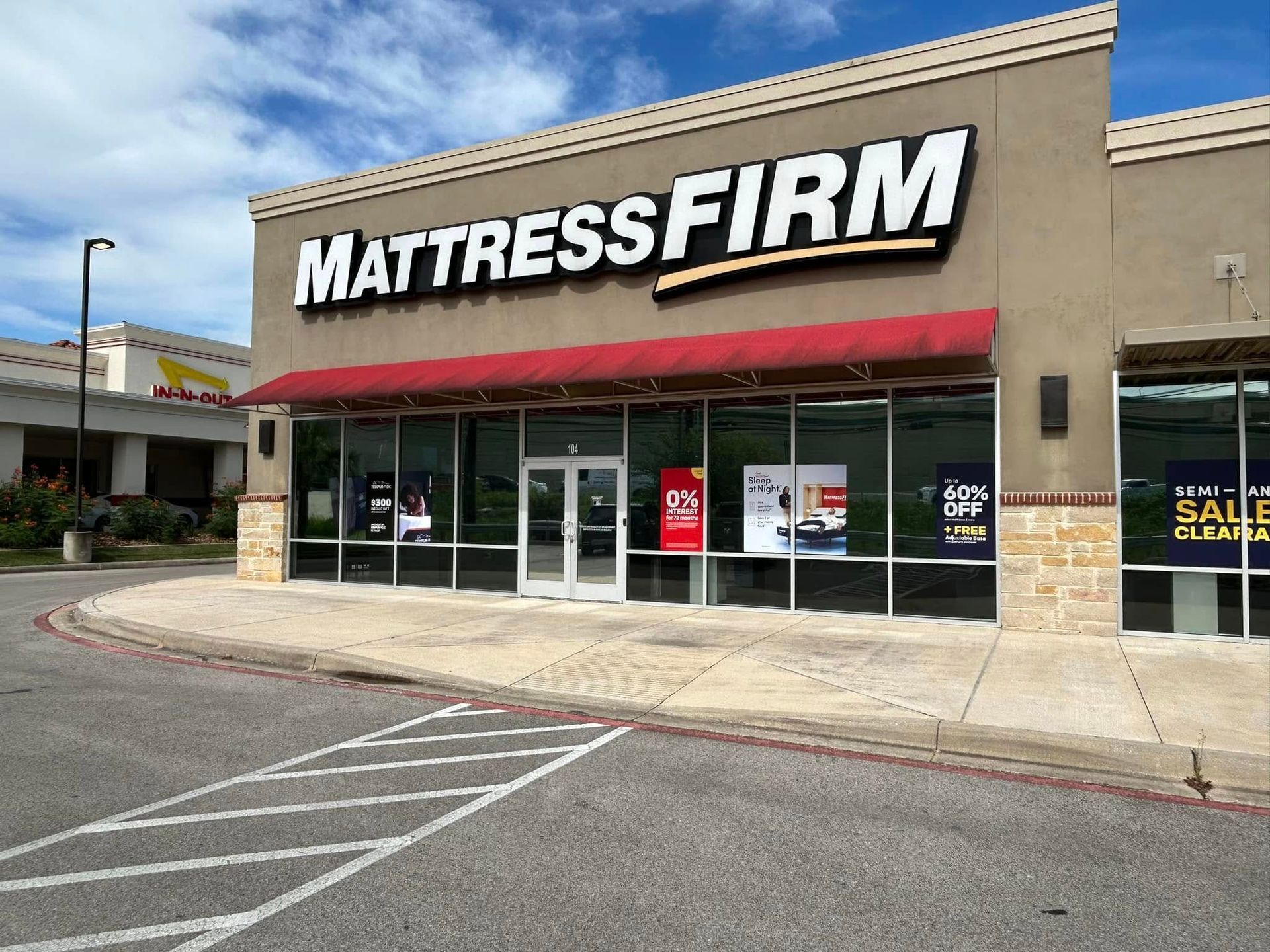 Mattress Firm store exterior with red awning. The building has a beige facade and large glass windows.