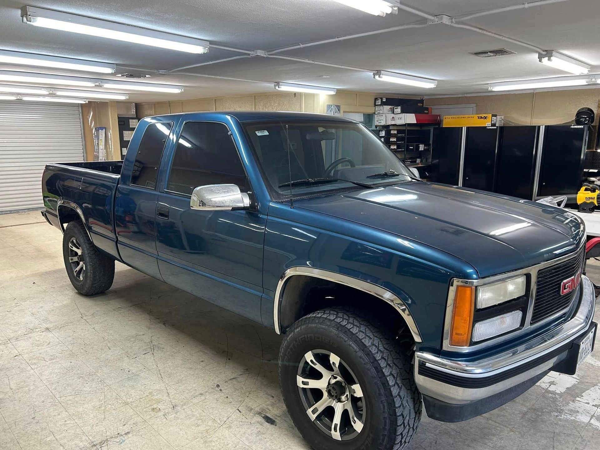 Blue GMC pickup truck in a garage, dark tinted windows, silver trim.