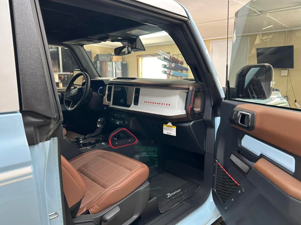Interior of a light blue Ford Bronco, showing brown leather seats and dashboard, black steering wheel.