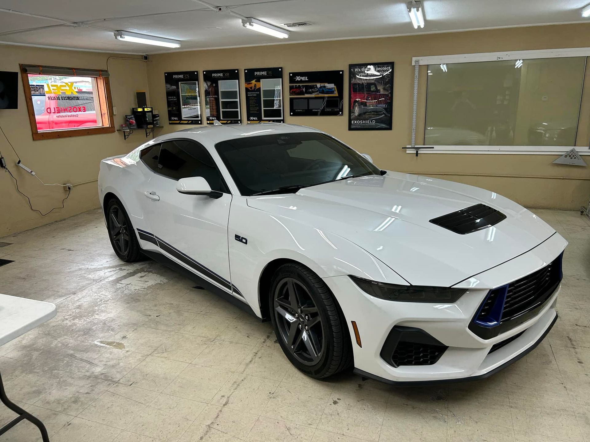 White Ford Mustang in a shop, with tinted windows and black accents.