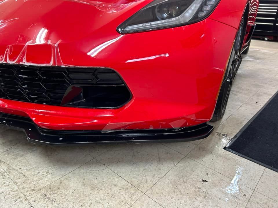 Red sports car, close-up front. Black trim. Protective film applied. Garage setting.