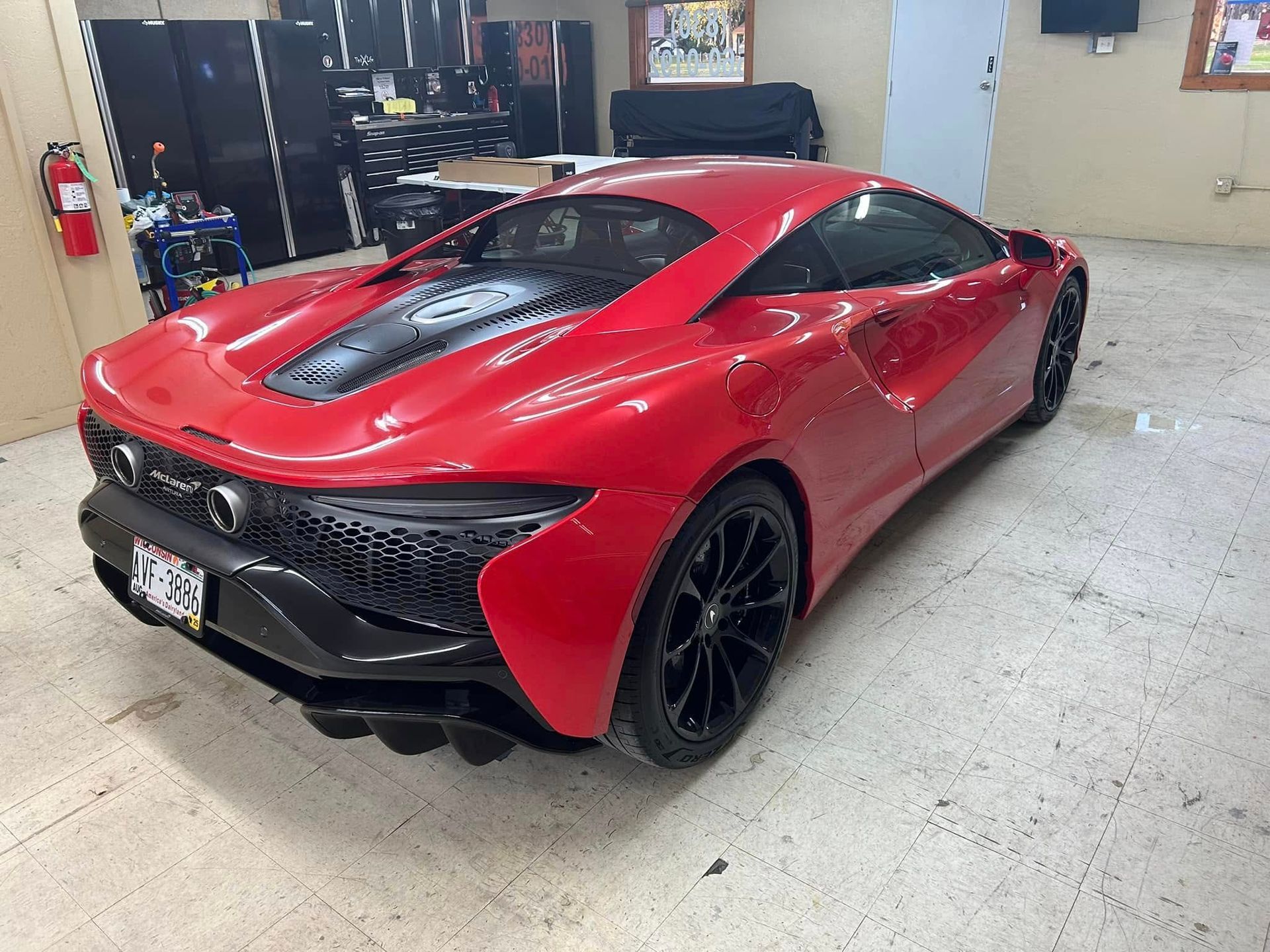 Red McLaren sports car in a garage with black rims.