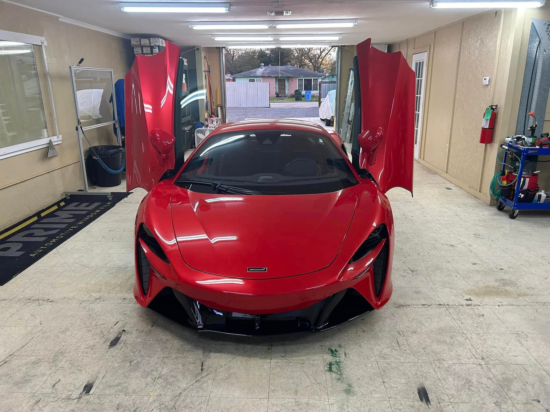 Red sports car with doors open in a garage.