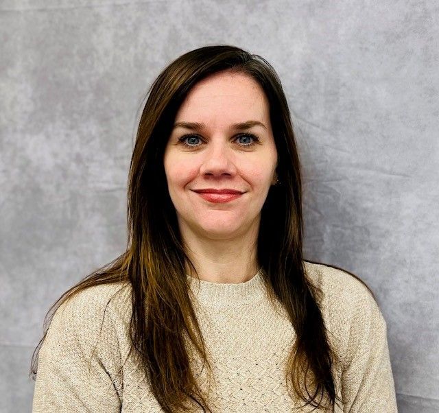 Portrait of a smiling woman with long dark hair against a gray backdrop