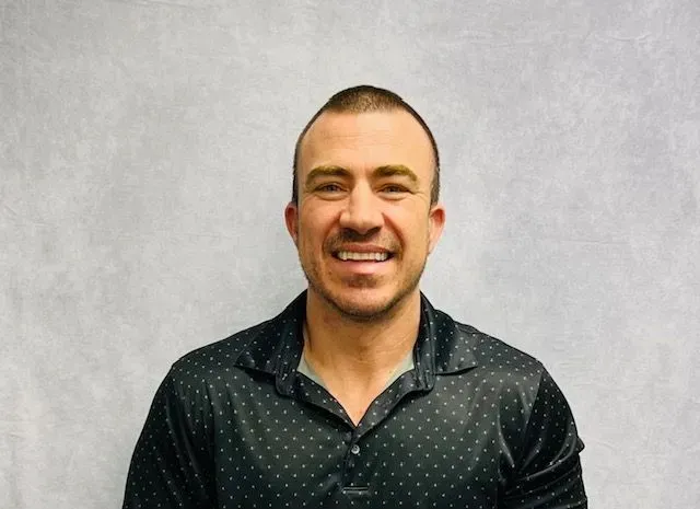 Smiling man in a dark patterned shirt against a light gray background
