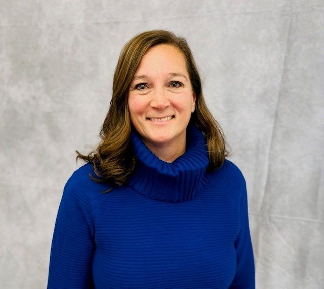 Smiling woman in a royal blue turtleneck against a gray backdrop