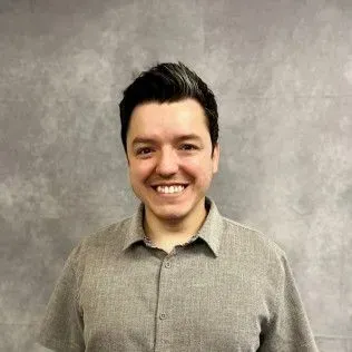 Smiling person in a gray button-up shirt against a plain gray backdrop