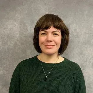 Woman with short dark hair wearing a green sweater and necklace against a gray backdrop