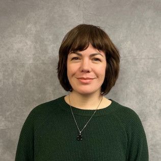 Portrait of a person with short dark hair wearing a green sweater against a gray backdrop