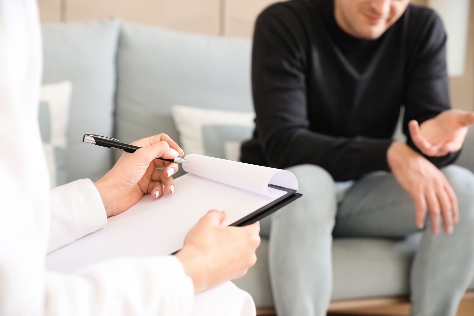 Therapist taking notes while speaking with a seated client on a sofa
