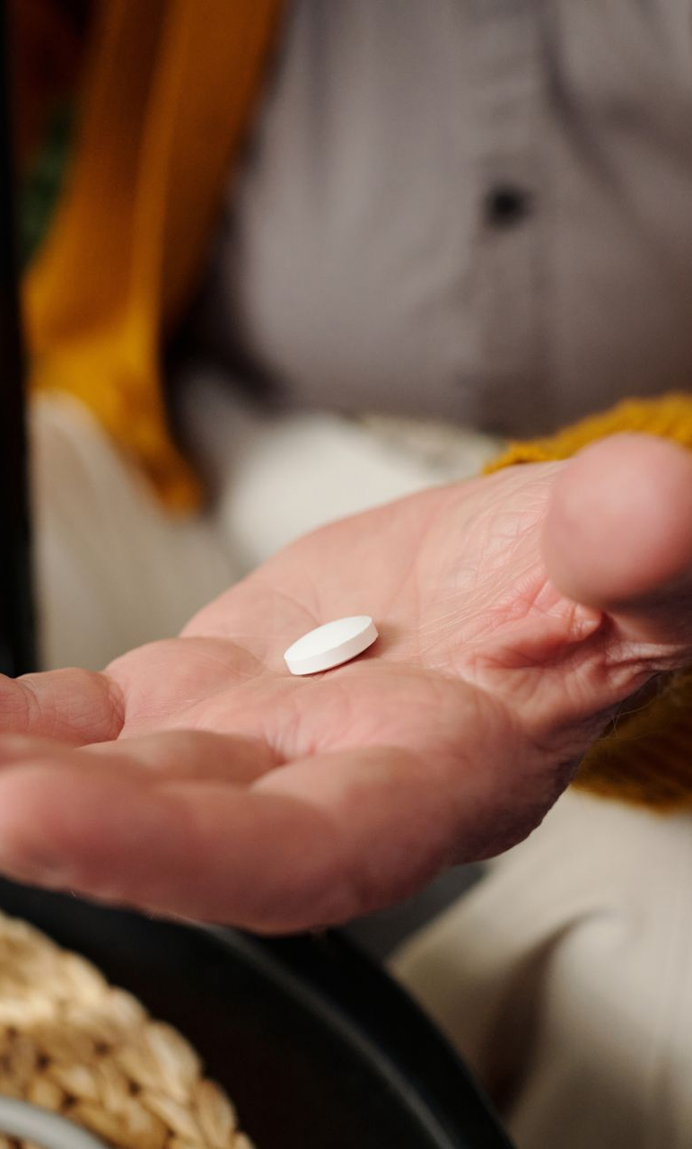 Palm holding a small white pill, with a blurred person in the background