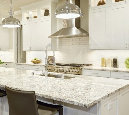 A white kitchen with marble countertops and metal light fixtures