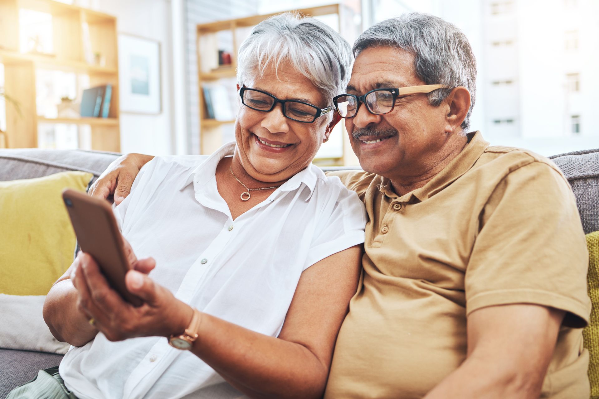 An elderly couple is sitting on a couch looking at a cell phone.