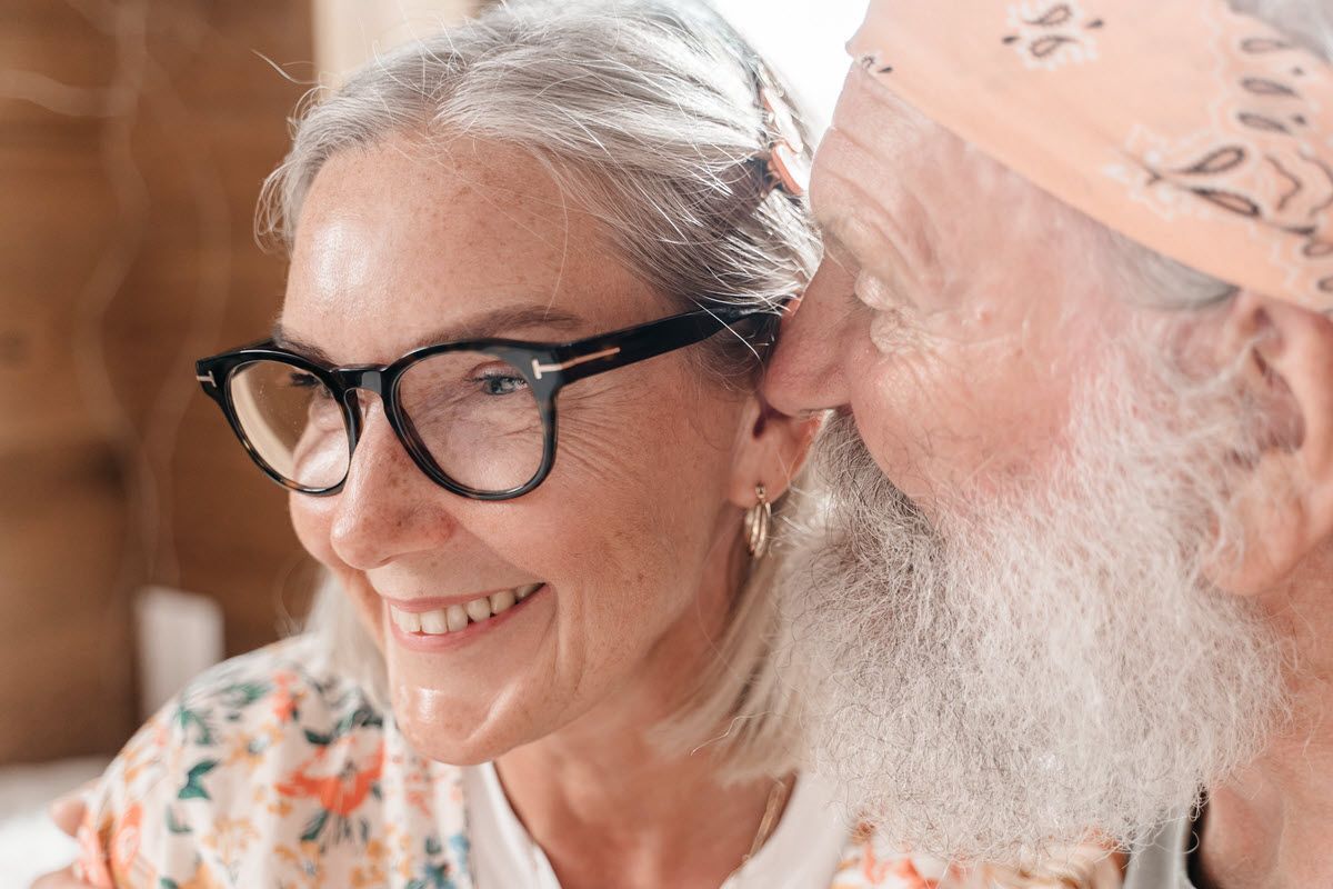 Smiling pair in close-up, one wearing glasses, sharing a warm moment indoors