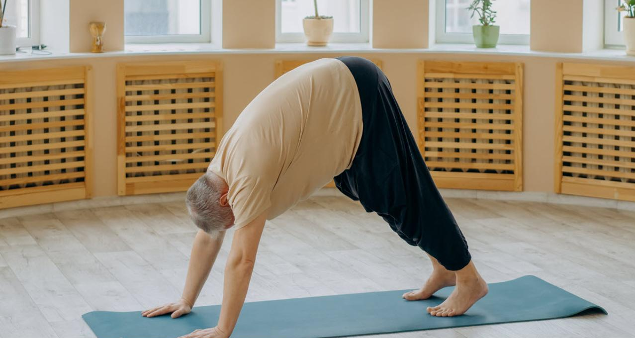 An older adult doing a downward dog yoga pose on a mat indoors.