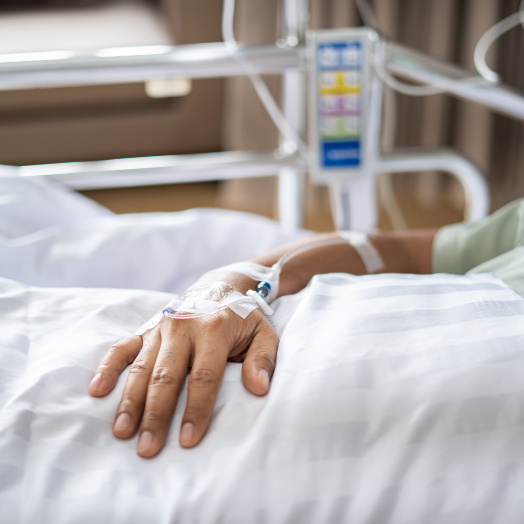 A person is laying in a hospital bed with an iv in their hand.