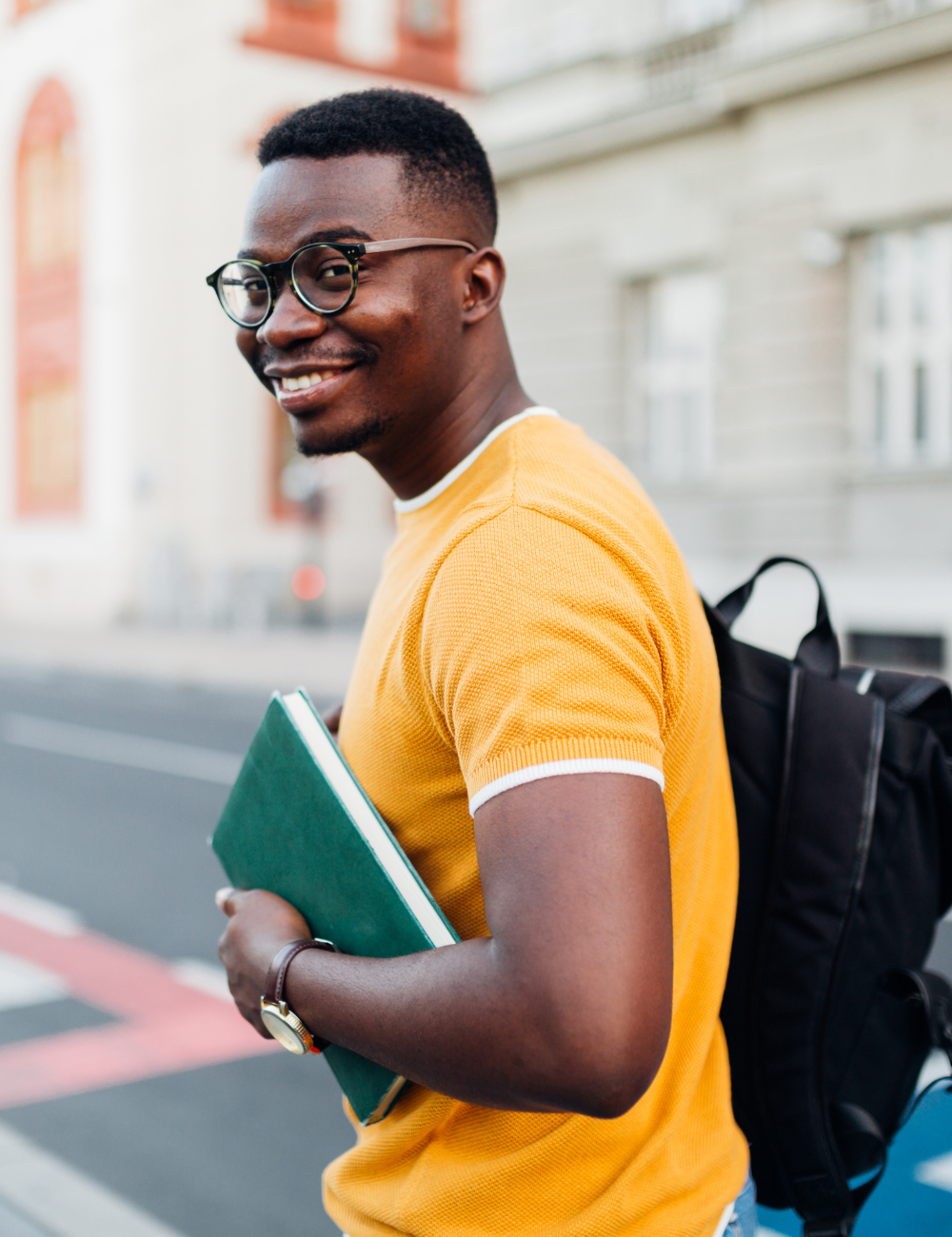 A man wearing glasses and a yellow shirt is holding a book and a backpack.