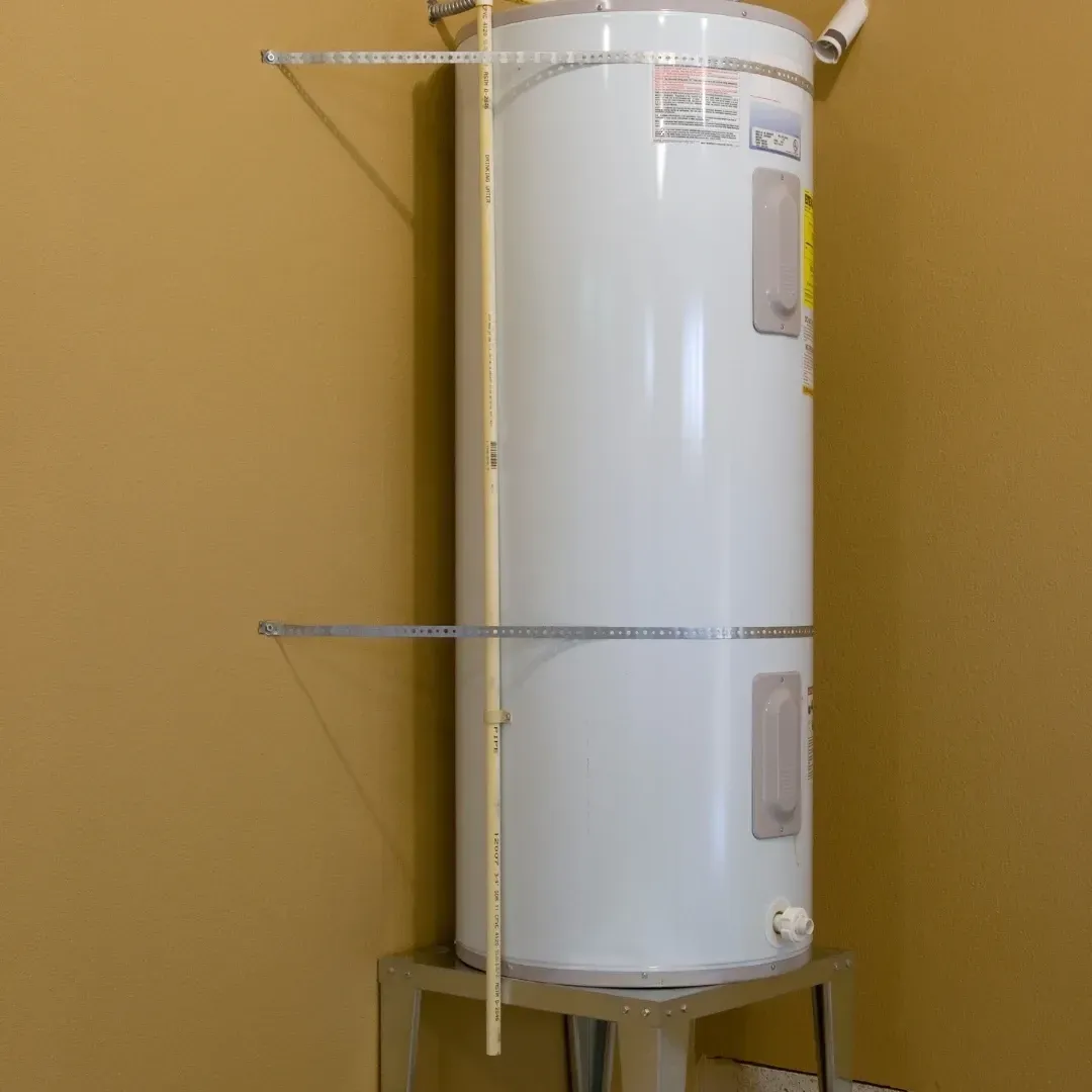 White water heater tank with metal support bars against a tan wall.