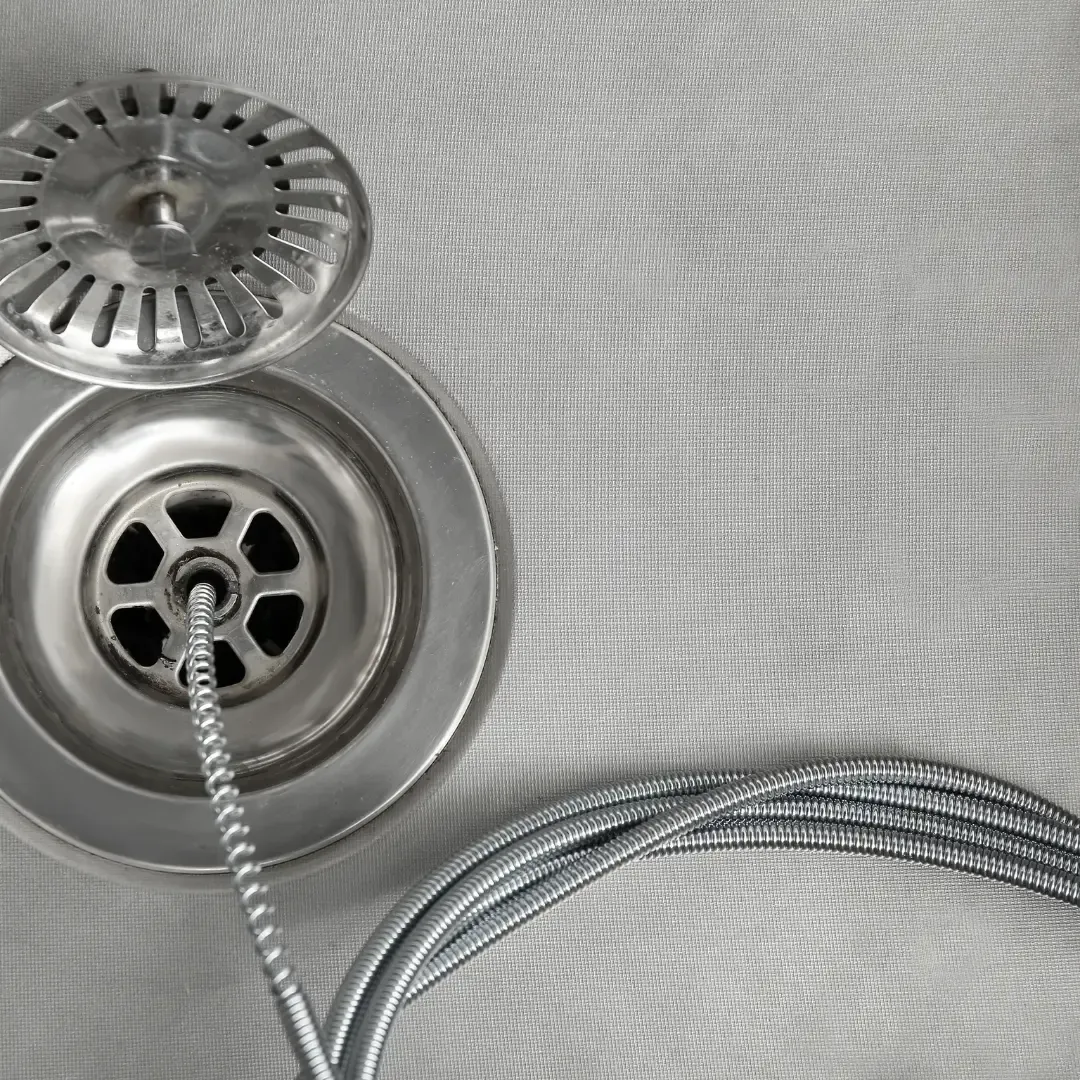 Stainless steel sink drain and strainer with braided hose on a light textured surface