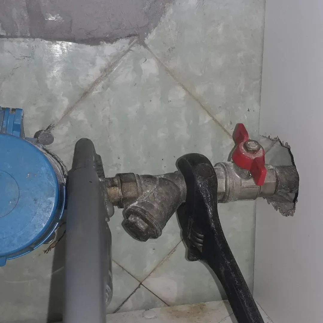 Close-up of plumbing valves and pipes on a tiled floor, with a red shutoff valve and blue cap.
