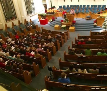 Wide view of a church or council chamber with seated audience facing a podium and empty choir chairs