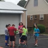 Group of people standing with bicycles in a driveway near a garage, chatting outdoors.