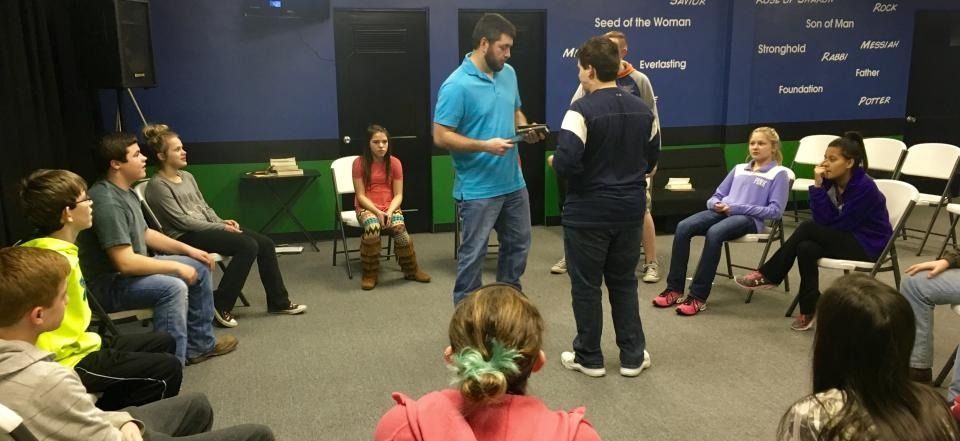 Group seated in a circle during a workshop, with two people standing and speaking at the center.