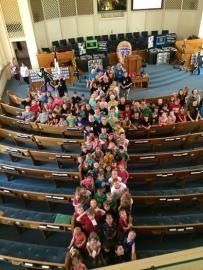 Large group seated in church pews, gathered around a central aisle in a sanctuary.