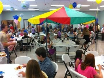 Indoor gathering with people seated around tables under a colorful red, yellow, and green canopy