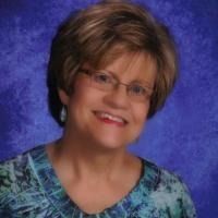 Smiling woman in glasses wearing a blue patterned top against a purple backdrop